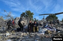 Distressed local residents sit at a site of a residential area heavily damaged by a Russian missile strike in Zaporizhzhia, Ukraine, Oct. 9, 2022.
