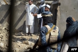FILE - Taliban officials stand in front of remnants of a suspected Islamic State hideout following an operation against Islamic State-Khorasan, the local chapter of the jihadist group, in Kandahar, Afghanistan, Nov. 15, 2021.