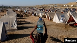 A girl carries a bottle of water she filled from nearby standing flood-waters at a camp for those displaced by recent flooding, in Sehwan, Pakistan, Sept. 30, 2022. 