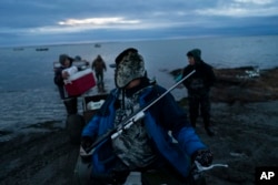 Wearing a seal fur hat made by his mother, Andrew Kakoona, 46, sits on an ATV with a hunting rifle secured on his chest as he and his relatives get ready for seal hunting in Shishmaref, Alaska, Tuesday, Oct. 4, 2022.
