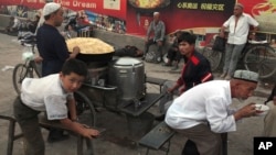 FILE - Uighurs rest near a food stall and Beijing Olympic Games billboards in Kashgar in China's western Xinjiang province, Aug. 30, 2016.