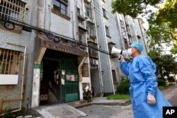 Seorang sukarelawan menggunakan megafon untuk berbicara dengan warga di sebuah gedung apartemen di Shanghai, China, 12 April 2022. (Xinhua News Agency via AP)