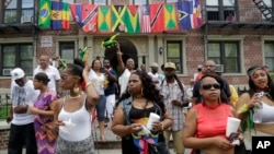 FILE - Flags representing Caribbean nations drape the front of a residential building as people gather outside to watch the annual West Indian Day Parade, celebrating Caribbean heritage, Sept. 1, 2014 in the Brooklyn borough of New York.