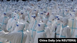 Petugas medis dengan pakaian APD melambai ke arah warga Changchun saat upacara perpisahan sebelum kembali ke Meihekou, tempat mereka membantu menangani wabah COVID-19 di Changchun, China, 12 April 2022. (Foto: via Reuters)