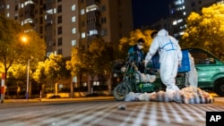 Deliverymen wearing protective suits carry bags of food at the gate of a residential community in Shanghai, April 11, 2022. 