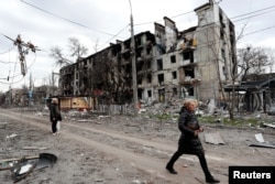 People walk past a residential building, which was heavily damaged in the southern port city of Mariupol, Ukraine during Russia's invasion of Ukraine, April 18, 2022.