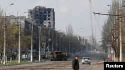 A local resident crosses a street damaged during Ukraine-Russia conflict in the southern port city of Mariupol, Ukraine, April 15, 2022.