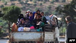 Warga Suriah yang mengungsi, duduk di belakang sebuah truk yang penuh dengan barang-barang saat melarikan diri di sepanjang jalan raya M4, di Ariha di provinsi Idlib, Suriah barat laut yang dikuasai pemberontak, 8 Juni 2020. 
