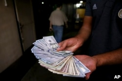 An illegal street money exchanger poses with his U.S. banknotes in downtown Tehran, Iran, Aug. 7, 2018.