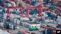 FILE - A cargo truck drives amid stacked shipping containers at the Yangshan port in Shanghai, China, March 29, 2018.