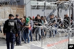 In this Nov. 19, 2018, file photo, people line up to cross into the United States from Tijuana, Mexico, seen through barriers topped with concertina wire at the San Ysidro port of entry in San Diego.