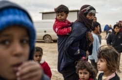 An elderly Syrian woman carries a toddler as others gather at the Washukanni camp for internally displaced persons (IDP) in the mainly Kurdish northeastern Syrian province of Hasakeh, Dec. 27, 2019.