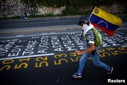 A demonstrator carries a Venezuelan flag as he runs next to a list of the victims of the violence during protests against Venezuela's president Nicolas Maduro government in Caracas, Venezuela, June 12, 2017.