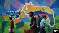Personas caminan junto a un mural que hace campaña a favor de un referéndum para pedir a los venezolanos que consideren la anexión de la región de Esequibo administrada por Guyana, en el barrio 23 de Enero de Caracas el 28 de noviembre de 2023.