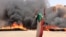 A protester wearing a Sudanese flag flashes the victory sign in front of burning tires and debris on Road 60, near Khartoum's army headquarters, in Khartoum, Sudan, June 3, 2019.