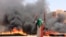 FILE - A protester wearing a Sudanese flag flashes the victory sign in front of burning tires and debris on road 60, near Khartoum's army headquarters, in Khartoum, Sudan, June 3, 2019.