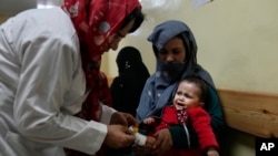 An Afghan woman holds her sick daughter as a nurse treats her in the malnutrition ward of the Indira Gandhi Children's Hospital in Kabul, Afghanistan, Feb. 24, 2022. 