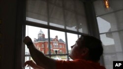 Brian Lambert, owner of Scoops, a coffee and sweets shop, opens up the windows of his business across the street from the Forsyth Courthouse as he gets ready to reopen next week, April 22, 2020, in Forsyth, Ga. The Monroe County Commission…
