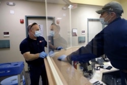In this Wednesday, May 20, 2020 photo carpenters John Mackie, of Canton, Mass., left, and Doug Hathaway, of Holliston, Mass., right, apply trim to a newly installed plastic barrier in an office area, at Boston University, in Boston. (AP Photo/Steven Senne)