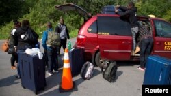 FILE - A refugee family claiming to be from Haiti take their luggage from their taxi as they arrive at the U.S.-Canada border on Roxham Road in Champlain, New York, August 3, 2017.