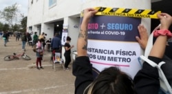 Una mujer sostiene un cartel que llama a mantener el distanciamiento social en un centro de votación en Santiago, Chile, durante un referendo para decidir si se cambia la constitución. Domingo 25 de octubre de 2020.
