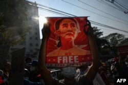 FILE - A protester holds up a poster featuring Aung San Suu Kyi during a demonstration against the military coup at in front of the Central Bank of Myanmar in Yangon, Feb. 15, 2021.