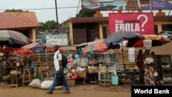 FILE – A sign urging precautions to fight the spread of Ebola hangs over a market in Guinea's capital, Conakry, Dec. 3, 2014. (Dominic Chavez/World Bank)