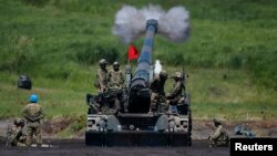 FILE - Japanese Ground Self-Defense Force soldiers fire a self-propelled howitzer during annual exercises near Mount Fuji at Higashifuji training field in Gotemba, west of Tokyo, Aug. 19, 2014.