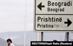 Dua perempuan berjalan di dekat rambu lalu lintas yang menunjukkan arah Ibu Kota Serbia Beograd dan Ibu Kota Kosovo Pristina di pintu masuk Kota Mitrovica di utara yang terbagi secara etnis, 9 Desember 2007. (Foto: Reuters)