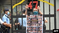 Seorang pengunjuk rasa berdiri di balik jeruji penjara tiruan dengan foto 47 tokoh pro-demokrasi yang dipenjara di Hong Kong, 19 September 2021, sebagai ilustrasi. (Foto: AFP)