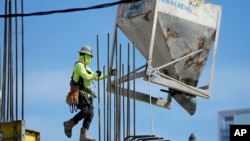 A worker guides a bin into position at a construction site, Jan. 24, 2023, in Miami.