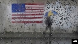 FILE - A pedestrian carries an umbrella while walking past a painting of an American flag in San Francisco, Jan. 11, 2023.