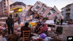 People sit and stand around a collapsed buildings in Golbasi, in Adiyaman province, southern Turkey, Feb. 8, 2023.