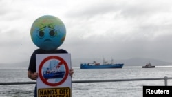 A member of Extinction Rebellion holds up a placard as the 'Akademik Alexander Karpinsky', a Russian polar explorer ship, arrives in Cape Town harbor, South Africa, Jan. 28, 2023. 