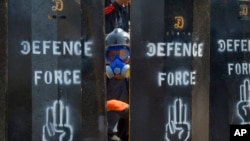 FILE - An anti-coup protester peeps from makeshift barricades in Yangon, Myanmar, March 11, 2021. Myanmar's military government has been accused of increasingly using battlefield weapons against peaceful protesters and conducting systematic, deliberate killings. 