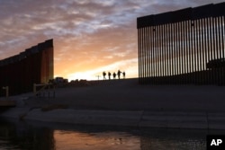 FILE - A pair of migrant families from Brazil pass through a gap in the border wall to reach the United States after crossing from Mexico to Yuma, Ariz., to seek asylum, June 10, 2021.
