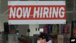 In this May 7, 2020, photo, a man wearing a mask walks under a Now Hiring sign at a CVS Pharmacy in San Francisco. California.