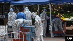 Para pekerja yang mengenakan pakaian hazmat tampak memeriksa makanan yang disiapkan oleh pemerintah lokal setempat untuk dikirimkan kepada para warga di Distrik Jing'an, Shanghai, yang kini menjalani lockdown pada 10 April 2022. (Foto: AFP/Hector Retamal)