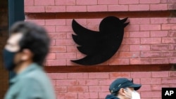FILE - People wearing face masks during the coronavirus pandemic walk by the Twitter logo outside the New York City headquarters in Manhattan, Oct. 14, 2020.