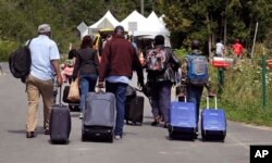 Members of a family from Haiti approach a tent in Saint-Bernard-de-Lacolle, Quebec, manned by Royal Canadian Mounted Police, as they haul their luggage down Roxham Road in Champlain, New York, Aug. 7, 2017.