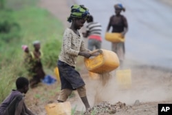FILE - A girl sifts roadside sand to separate the stones to sell as building material in Inchope, northern Mozambique.