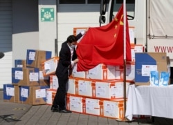 FILE - A man fixes the Chinese flag in front of boxes with protective suits and masks in Vienna, Austria, March 20, 2020.
