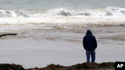 FILE - A man watches ocean waves crash at Seacliff State Beach in Aptos, California.