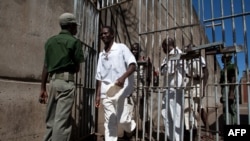 FILE - Prison Inmates walk past a prison guard at the Chikurubi Maximum security prison in Harare, Zimbabwe, May 20, 2015 during a tour by a parliamentary committee to assess the state of the nation's prisons where inmates widely complained of food shortages, over-crowding and inadequate food rations and diet. 