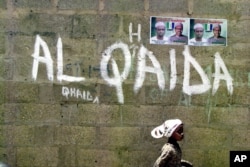 FILE - A girl walks past a wall with graffiti about the al-Qaida network in the northern city of Kano, Nigeria.