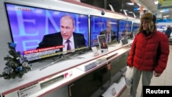 FILE - A customer stands near TV sets during the annual end-of-year news conference of Russian President Vladimir Putin at the "Pozitronika" electronic store in Russia's Siberian town of Divnogorsk.