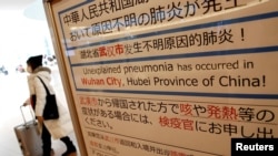 FILE - A woman wearing a mask walks past a quarantine notice about the outbreak of coronavirus in Wuhan, China, at an arrival hall of Haneda airport in Tokyo, Japan, Jan. 20, 2020.
