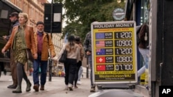 FILE - People walk past a bureau de change that displays the currency conversion rates, in London, Oct. 12, 2022. U.K. authorities are seeking public comment about launching a central bank digital currency that would equal standard currency. 