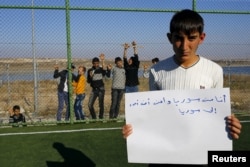FILE - Syrian refugee Mustafa Halebi, 16, holds a paper that reads in Arabic: "I am Syrian and I want to return to Syria" in Nizip refugee camp in Gaziantep province, Turkey, Dec. 13, 2015.