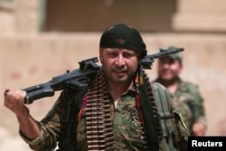 FILE - A Kurdish fighter from the People's Protection Units (YPG) carries his weapons as he walks the streets in the northeastern city of Hasaka, Syria, Aug. 21, 2016.